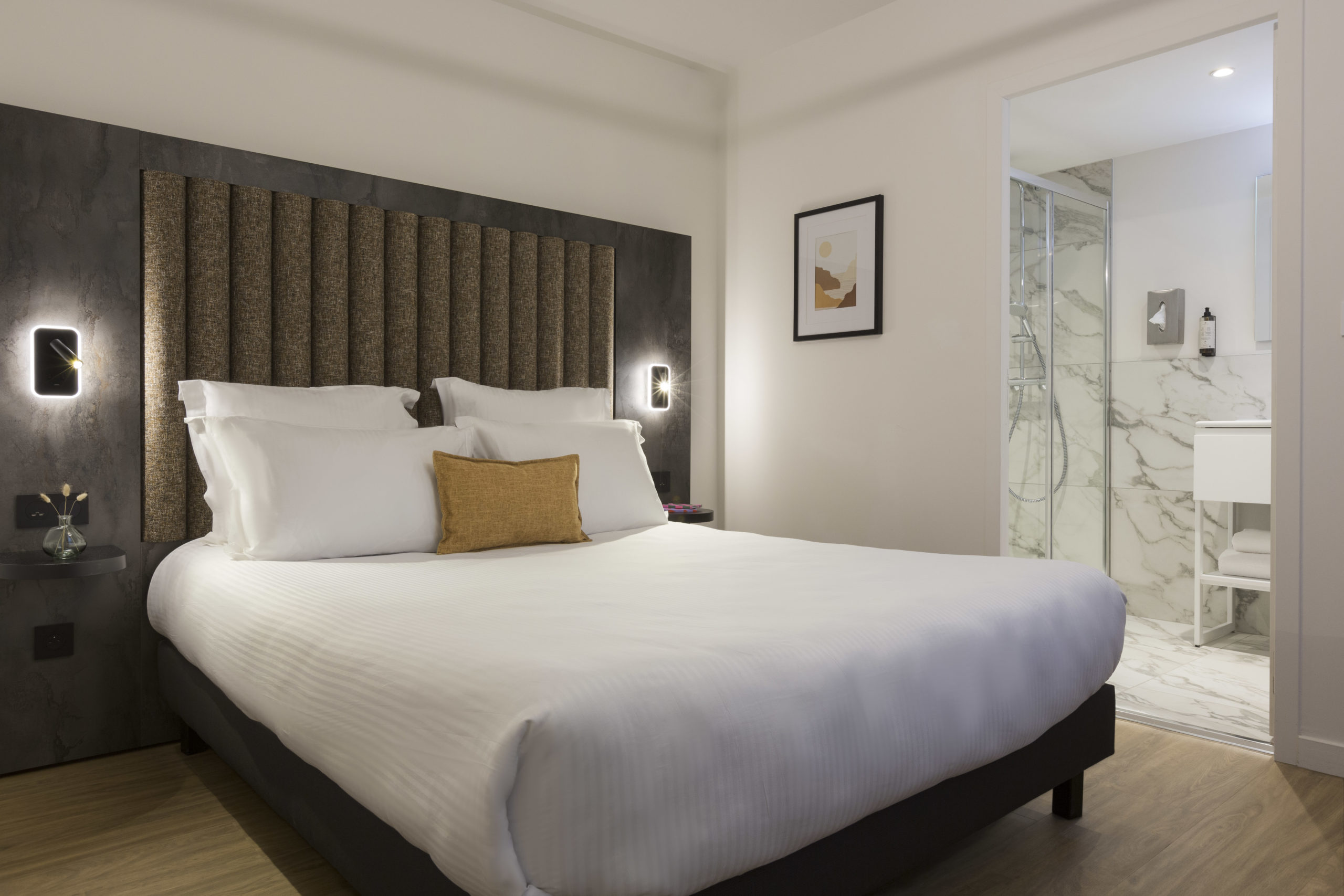 Chambre appartement 2 pièces avec lit double, tête de lit, liseuses et salle de bain ouverte au Nehô Suites Saint-Jean-de-Maurienne.