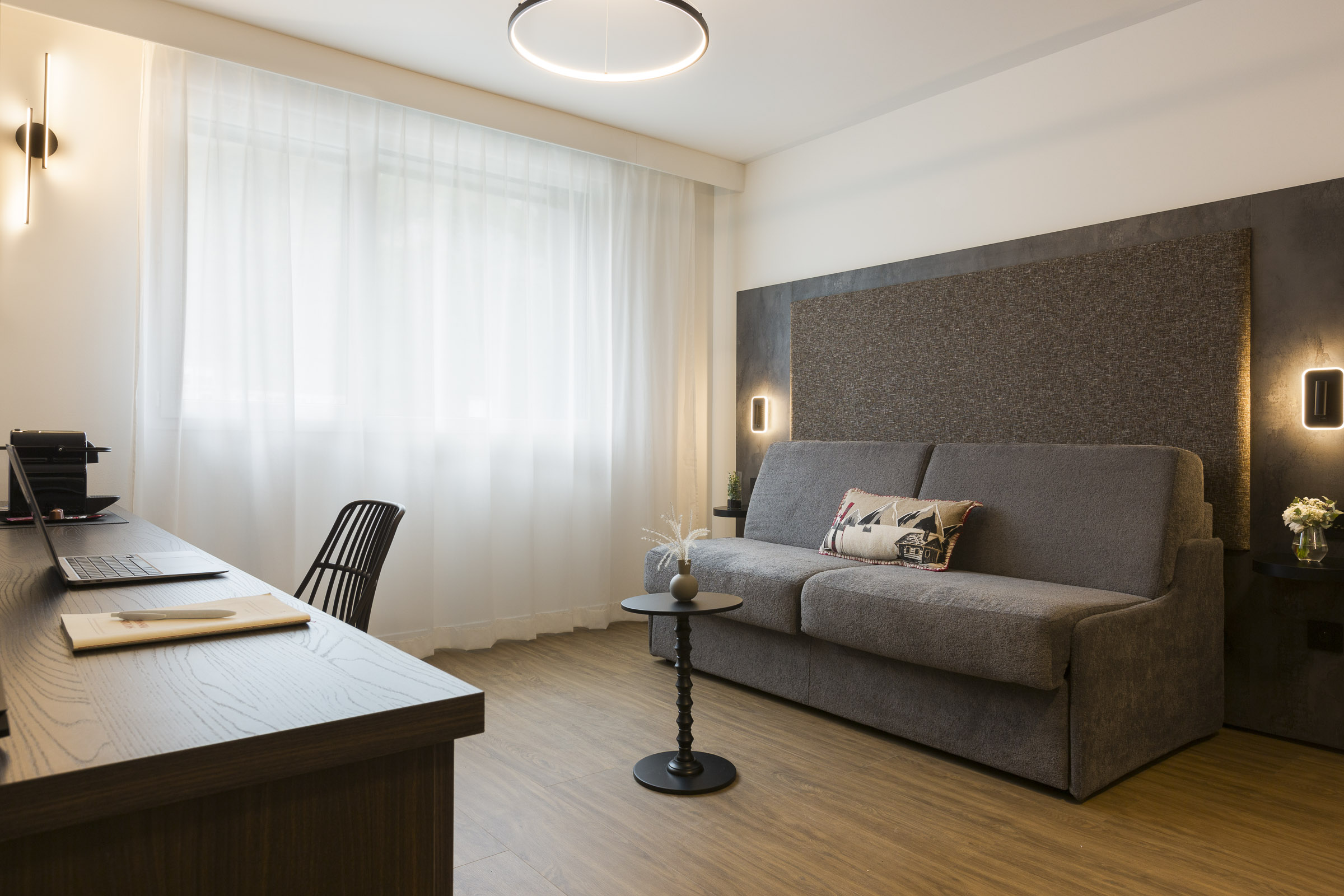 Studio supérieur configuration salon avec canapé lit, bureau, fauteuil et fenêtre lumineuse au Nehô Suites Saint-Jean-de-Maurienne.