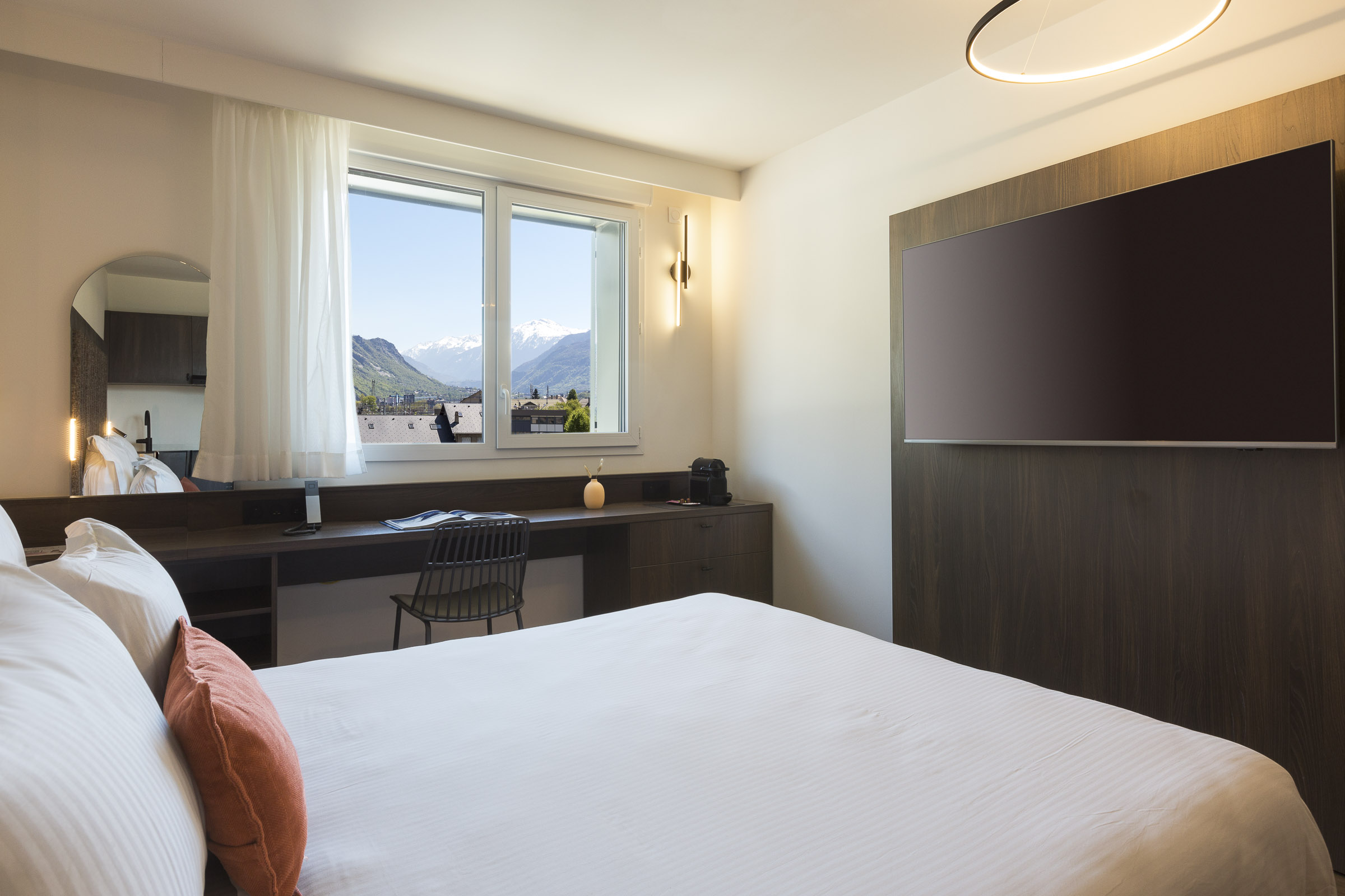 Studio classic avec lit double, bureau, télévision murale et fenêtre donnant sur les montagnes au Nehô Suites Saint-Jean-de-Maurienne.