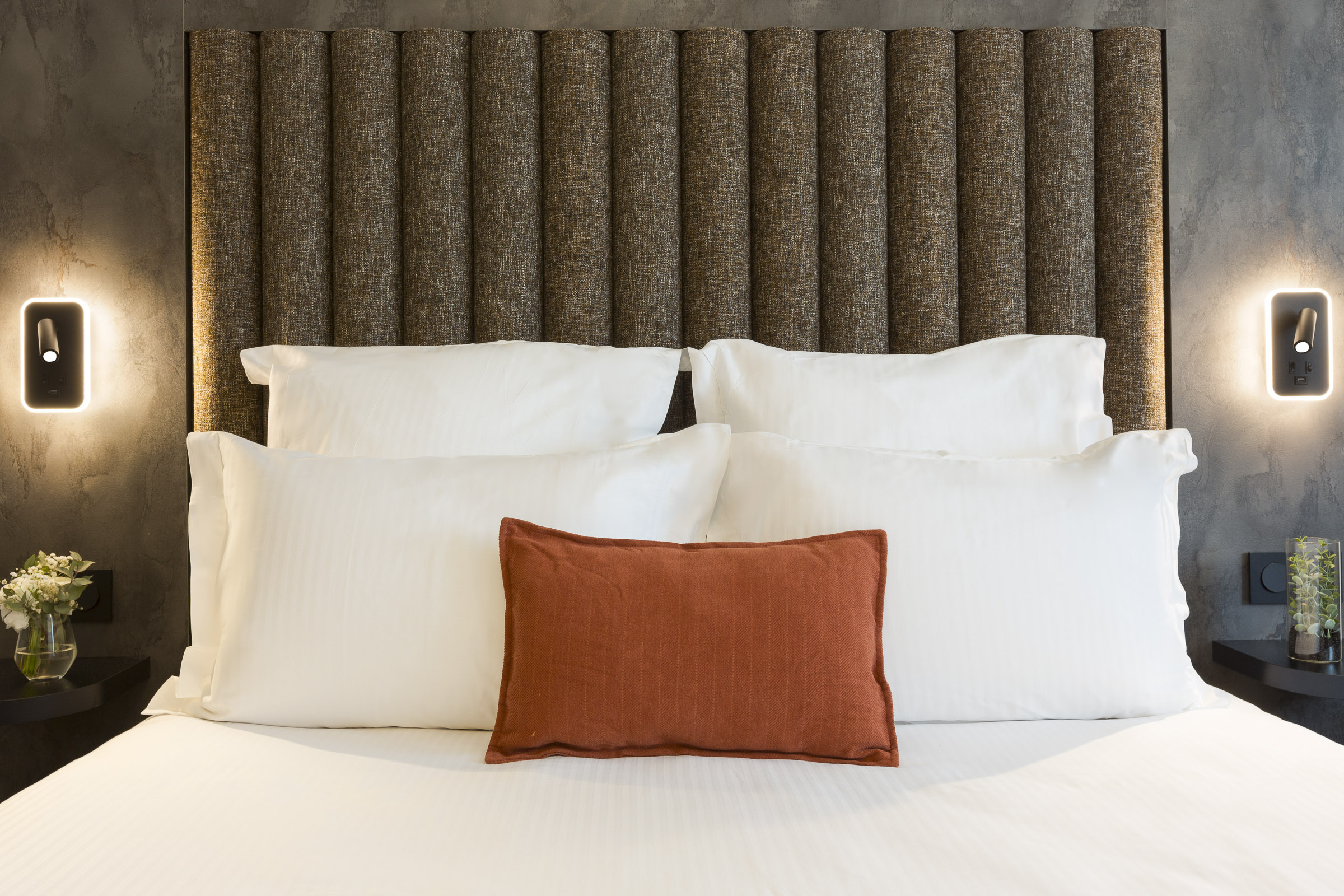 Lit double avec tête de lit textile et liseuses dans une chambre du Nehô Suites Saint-Jean-de-Maurienne.